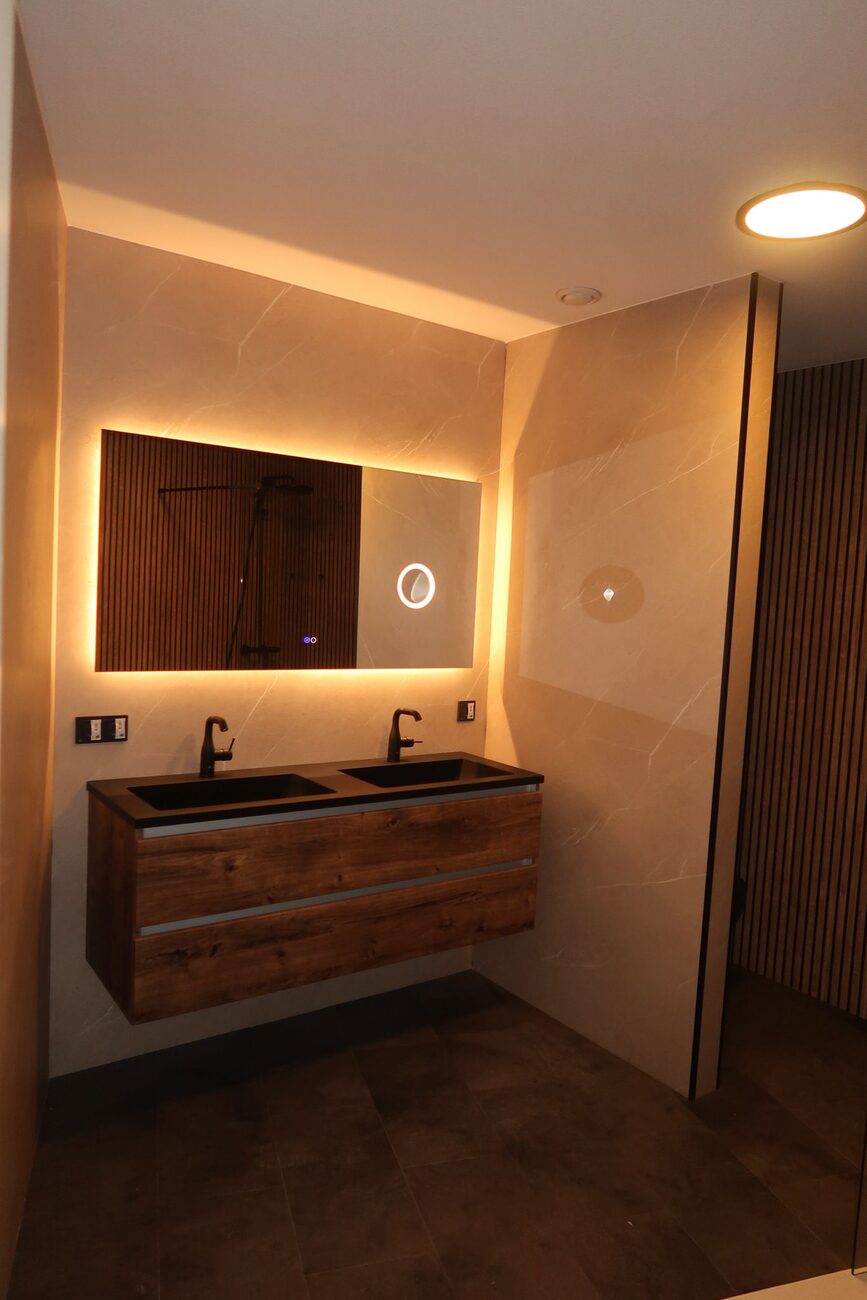 Moderne badkamer met dubbele wastafel en verlichte spiegel.